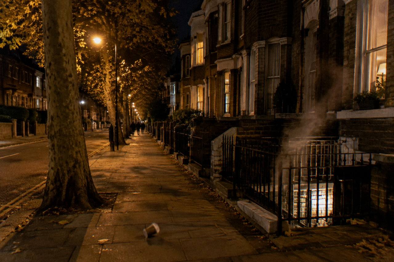 Goldhawk Road at night, plane trees lit amber over Victorian brick terraces in west London