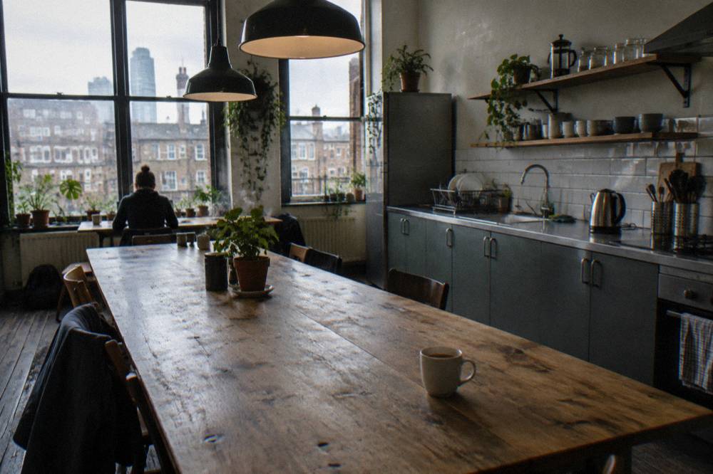 A hostel kitchen with a long wooden table, kettle and clean countertops