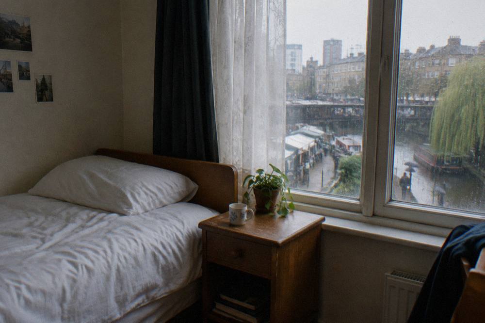 A made-up single bed with white sheets beside a wooden nightstand in a simple guest room
