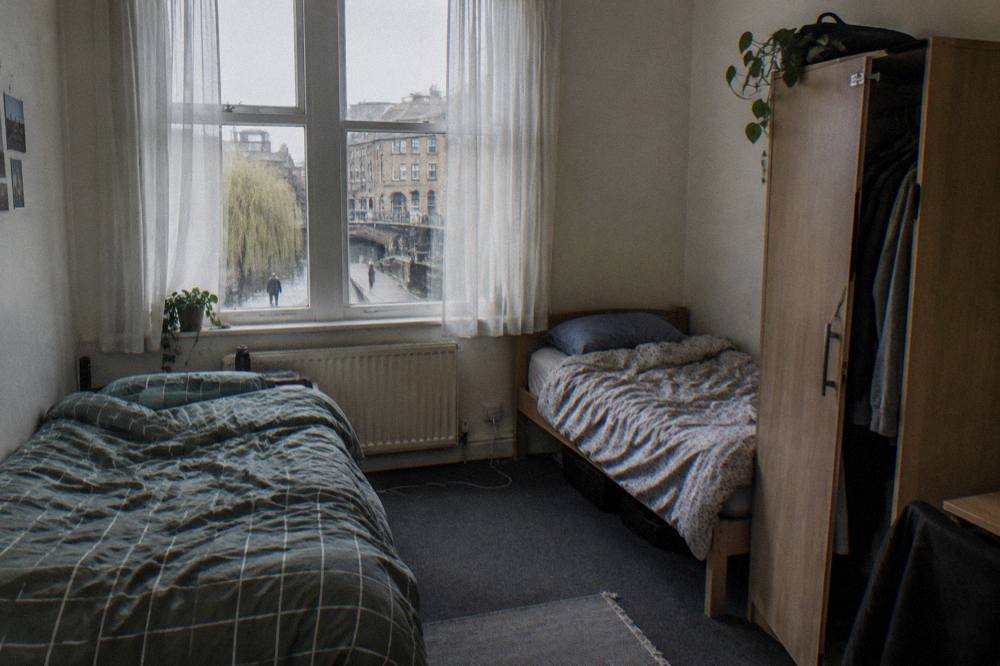 A twin hostel room with two single beds and a shared wardrobe beside a window