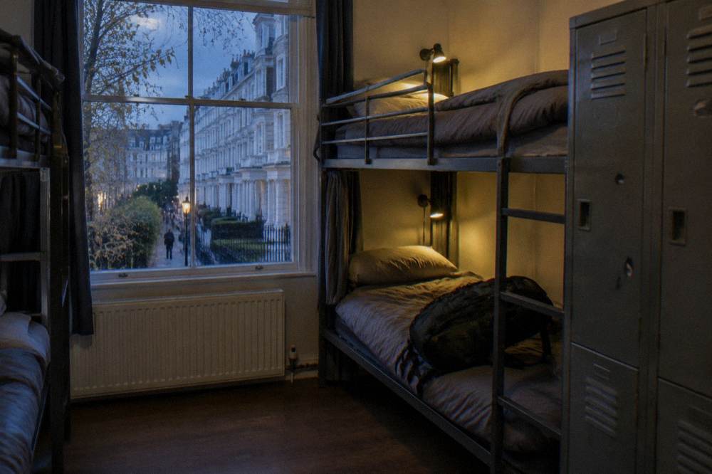 A bunk dorm room with four metal frame beds, reading lights and lockers along one wall