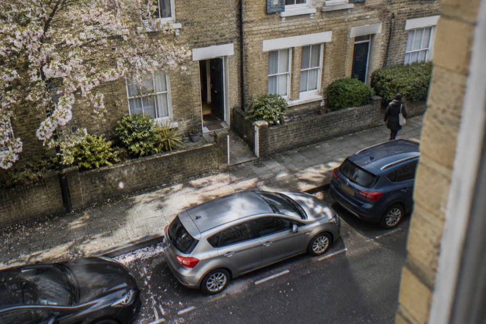 A narrow London residential street with brick terraced houses and parked cars