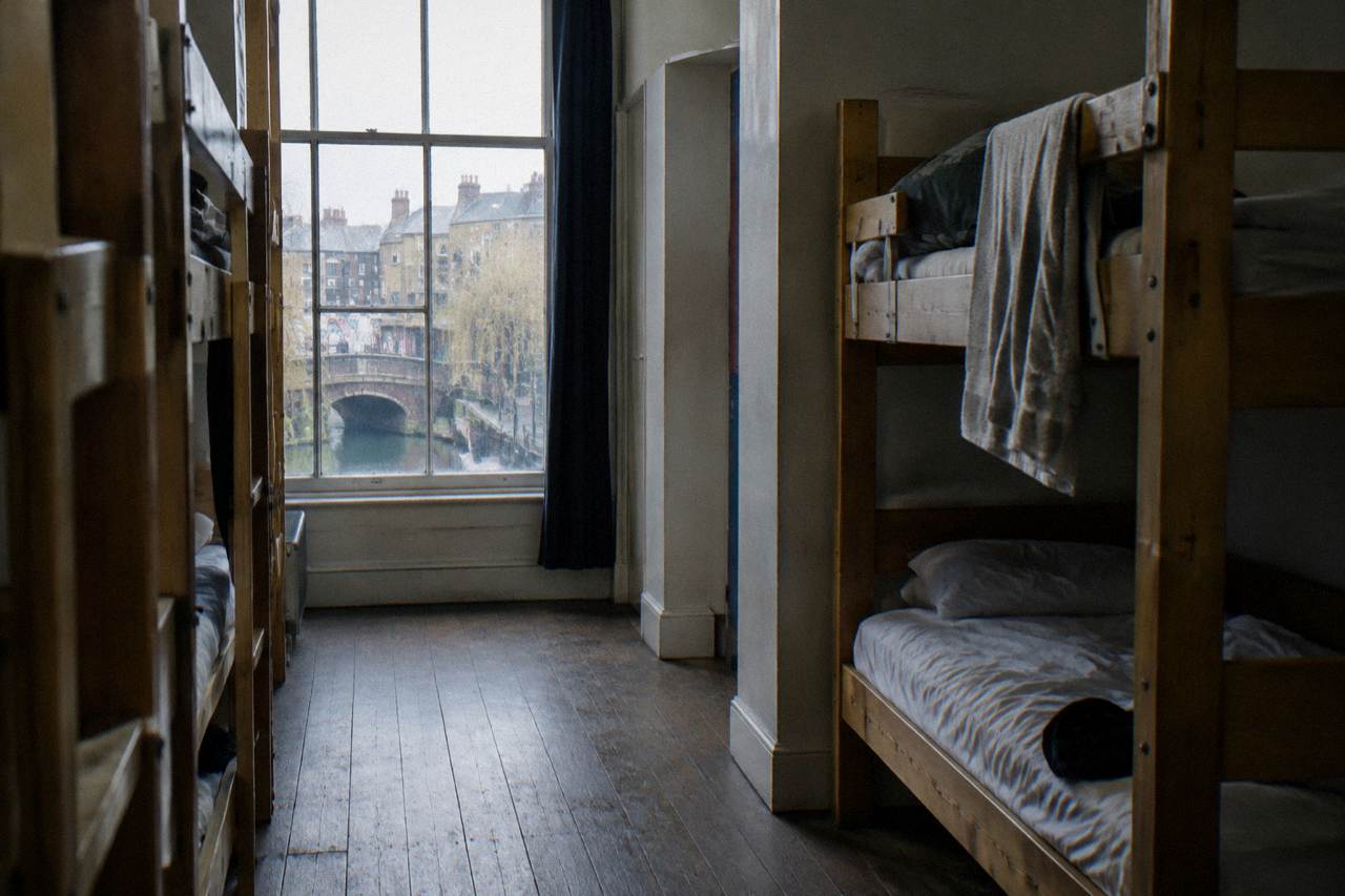 A quiet hostel dorm corridor with wooden bunks and a window onto a London street