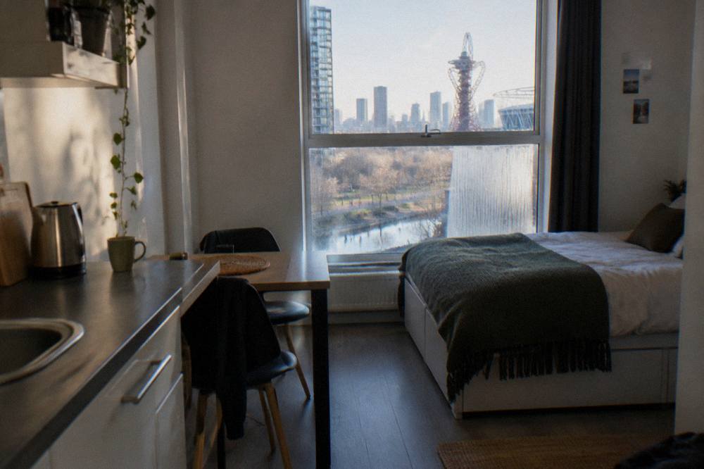 A studio room with a kitchenette, small dining table and double bed beside a tall window