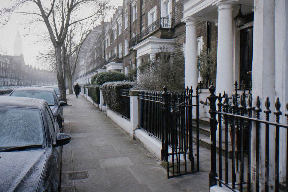 A London street of brick townhouses with white columned porches and parked cars