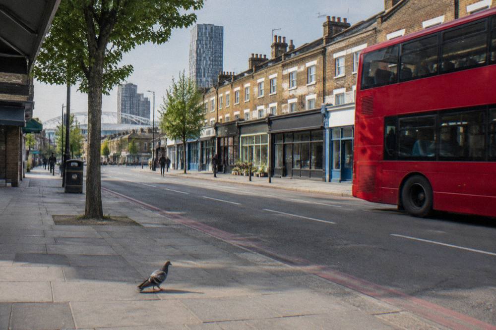 A London street of mixed shopfronts and brick terraces on a bright afternoon