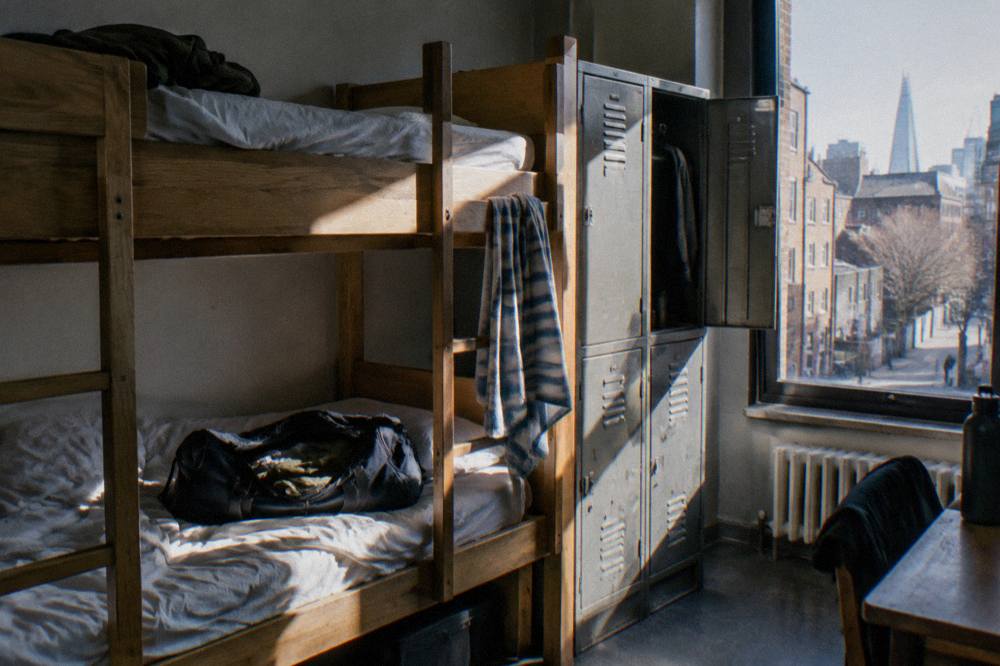 A bunk dorm room with wooden frames and a ladder beside lockers