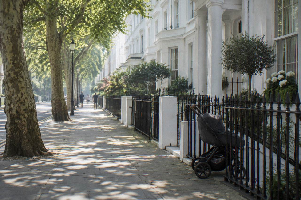 A London street with white stucco terraced houses and plane trees near a park