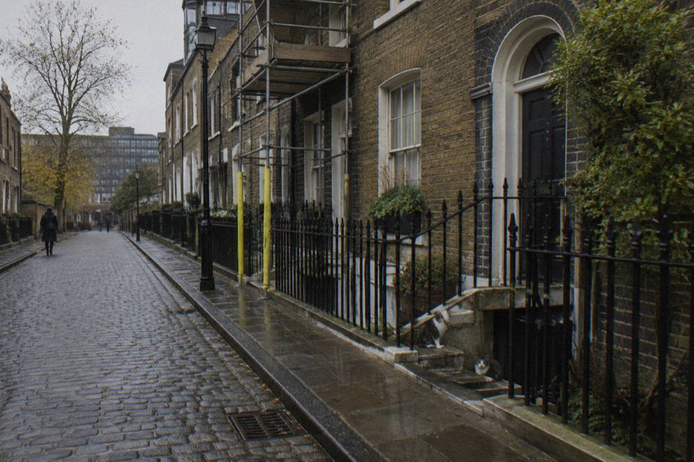 A narrow London residential street with brick terraced houses under an overcast sky