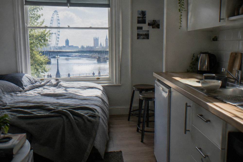 A studio room with a small kitchenette, two stools and a bed beside a window