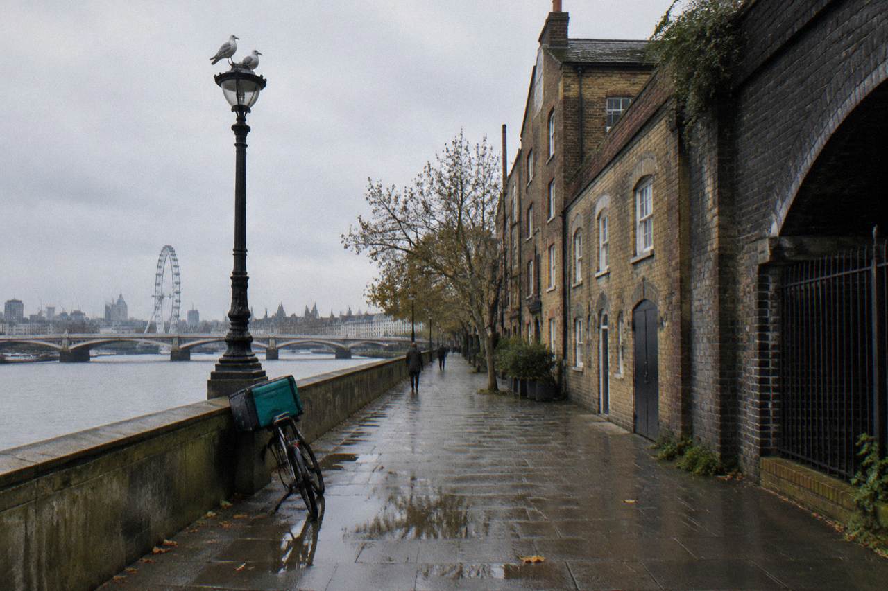 A London riverside street with brick buildings and a railway arch under an overcast sky