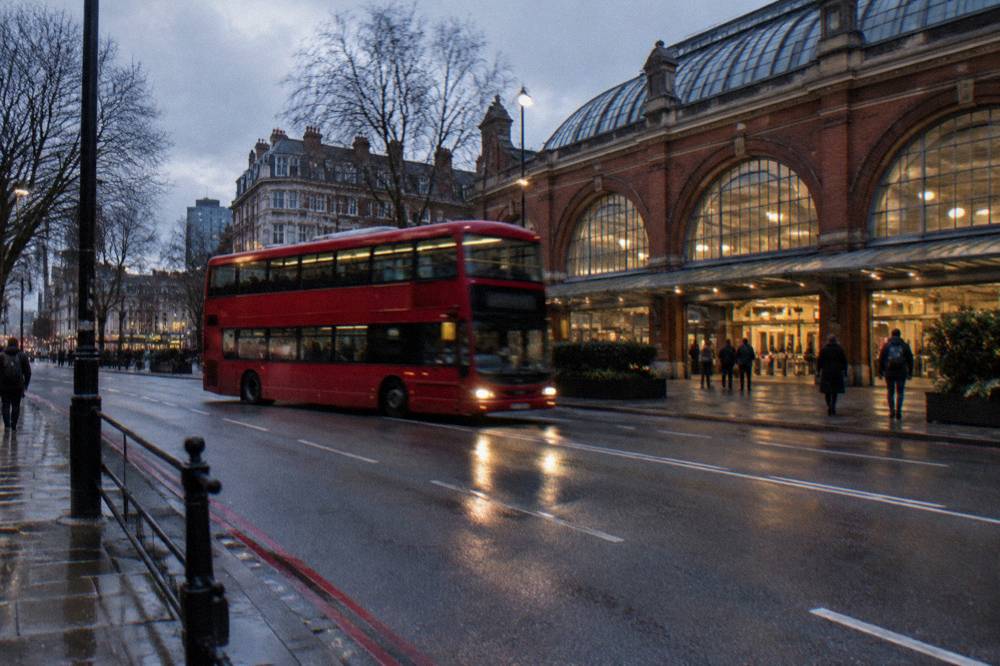 A London station exterior at dusk with a double-decker bus passing