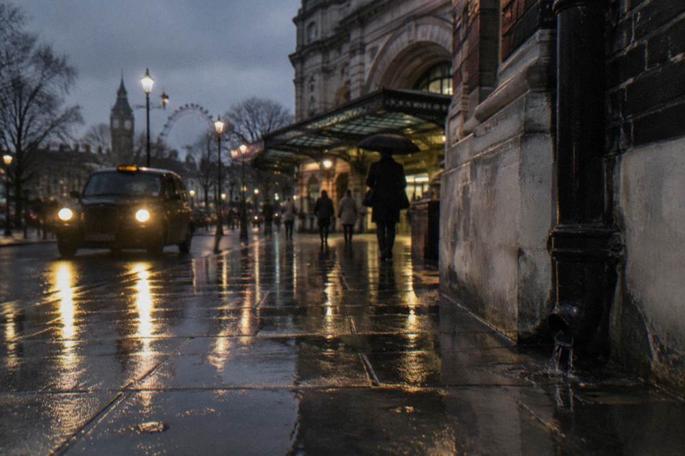 A rain-wet London street at night with black cab headlights reflecting on the pavement