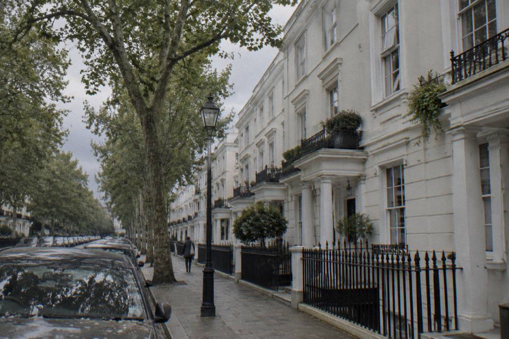 A London terrace street with white stucco facades and parked cars on a grey day