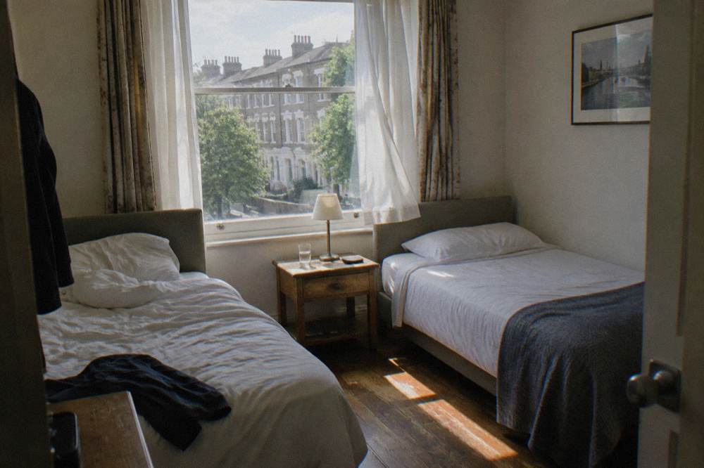 A small hotel twin room with two single beds, bedside table and window with curtains