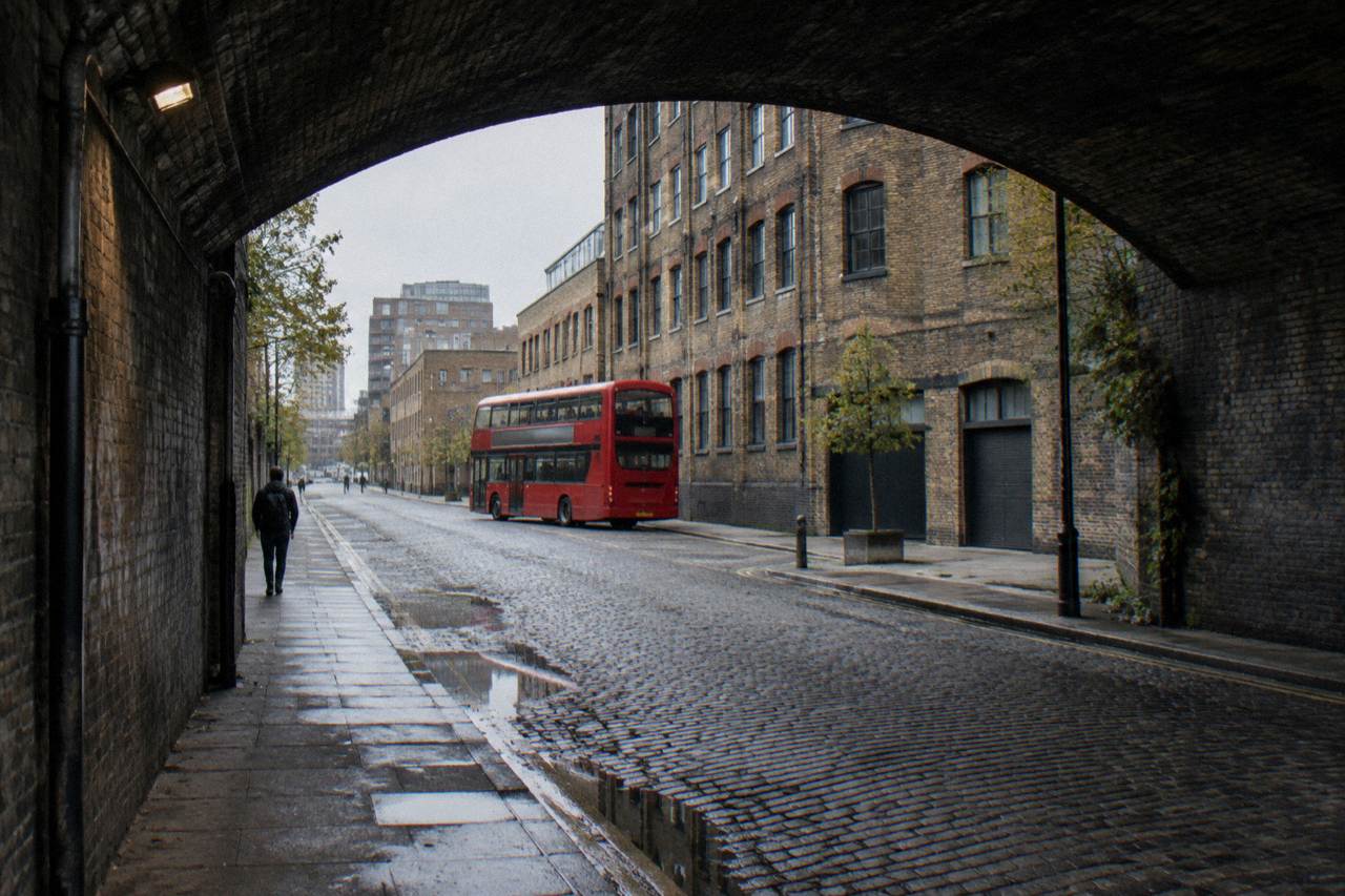 A London street of mid-rise brick buildings with a red bus passing under an overcast sky