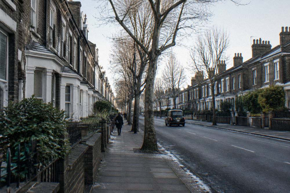 A view down a London residential street with brick terraced houses and trees along the pavement