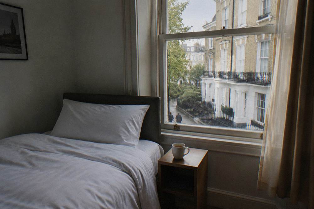 A made-up single bed with crisp white bedding beside a small bedside table