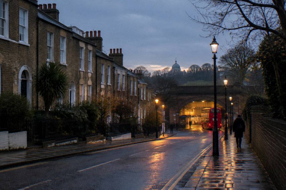 A London street at dusk with terraced buildings and a station entrance in the distance