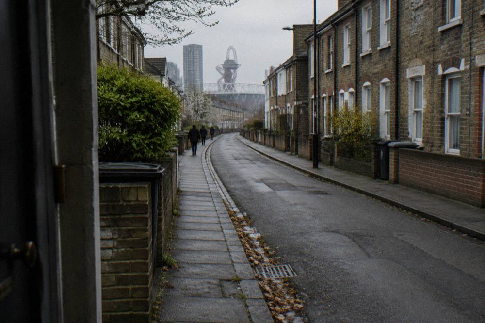 A narrow London street of brick terraced houses under an overcast sky