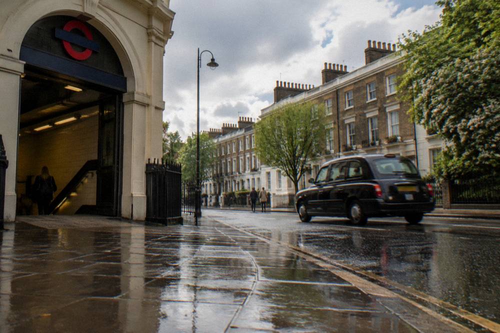 A station exterior on a London street with a black cab passing