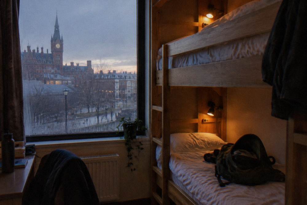 A hostel-style bunk dorm room with wooden frames and personal reading lights