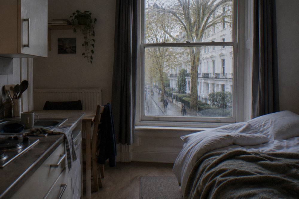 A studio room with a small kitchenette, double bed and window onto a London street