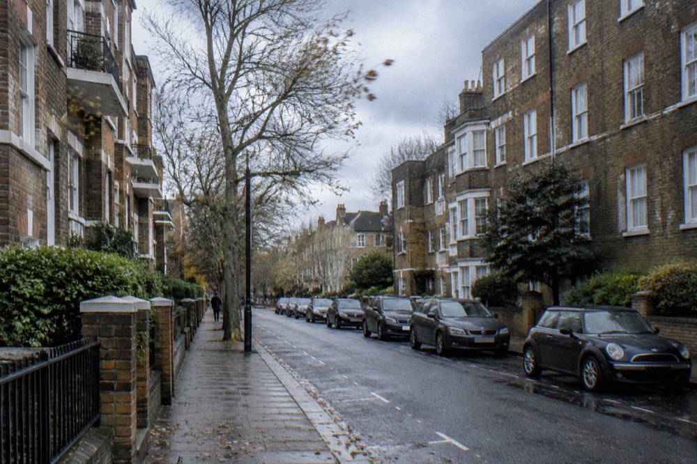 A narrow residential street with brick apartment buildings and parked cars in west London