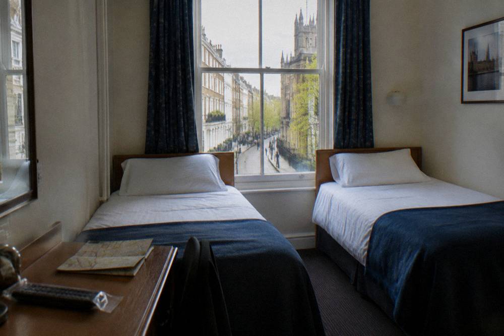 A twin hotel room with two single beds and bedside tables under a window