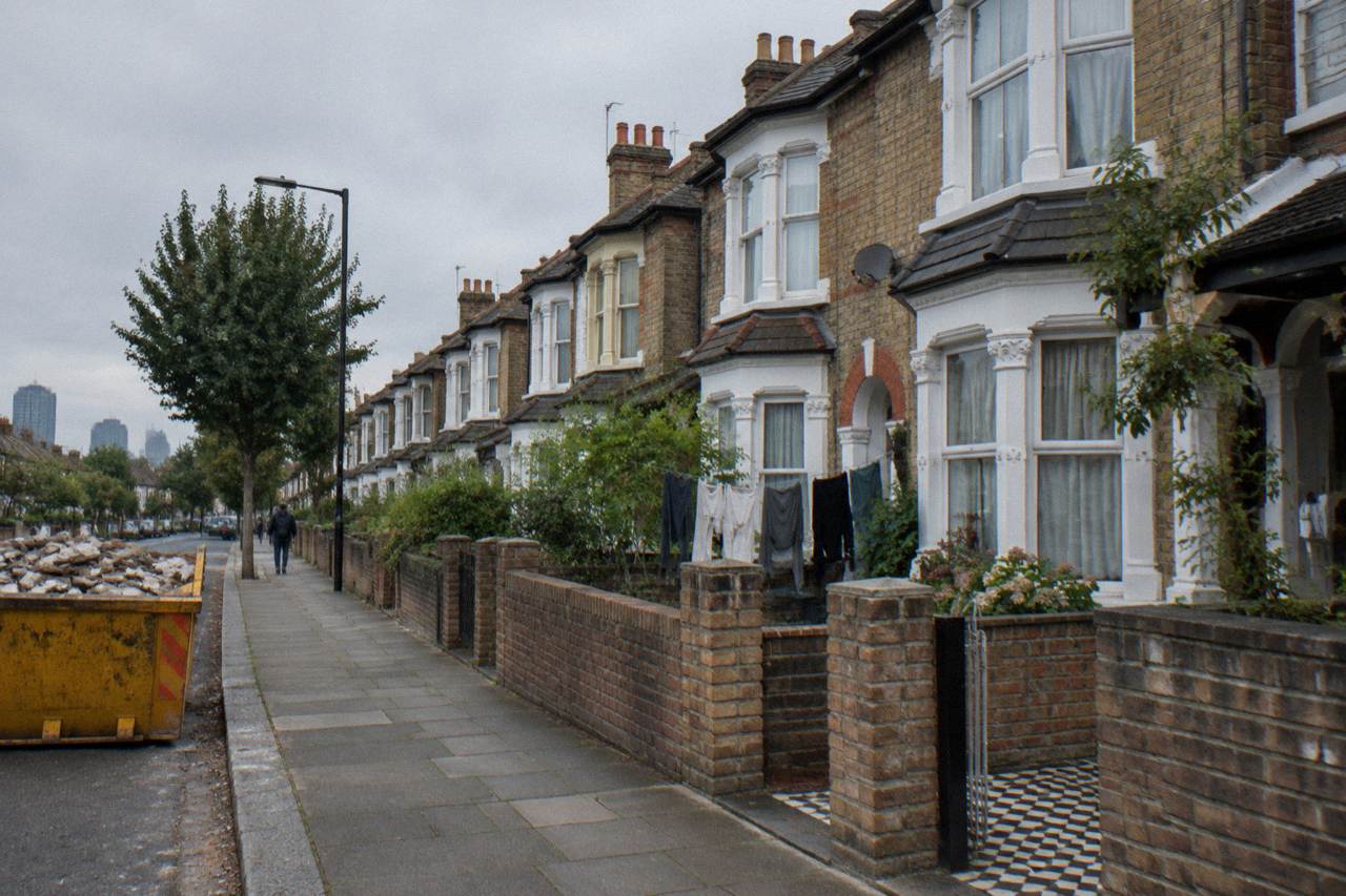 A residential street in East London with brick terraced houses under an overcast sky