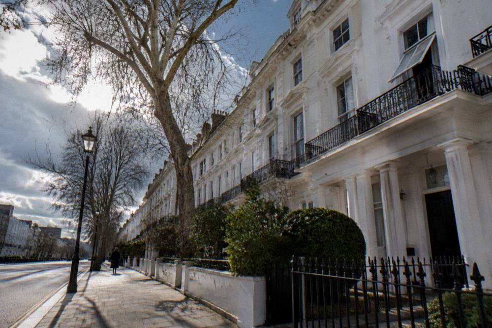 A London residential street of white terraced houses with a plane visible high overhead