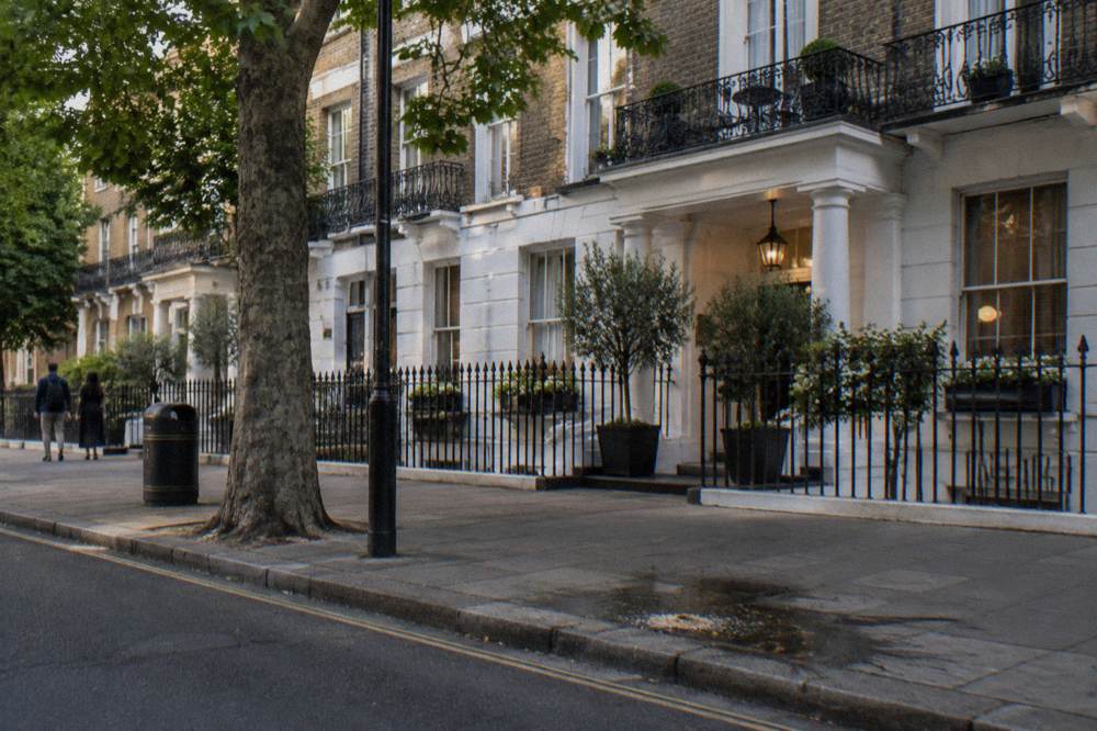 A traditional London hotel facade of brick and white trim on a tree-lined street