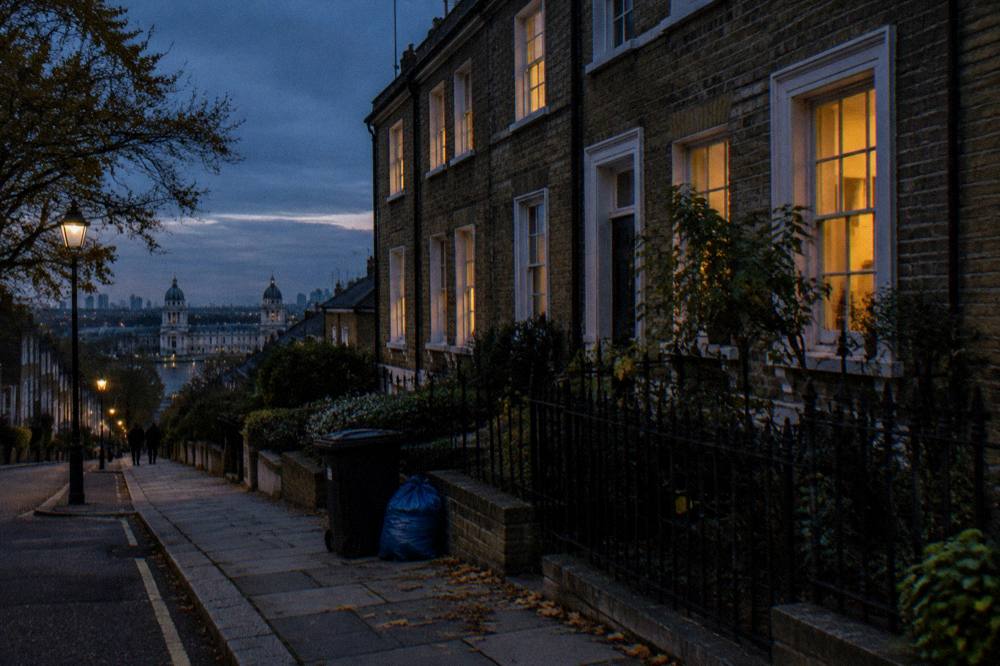 A quiet London terrace of brick townhouses at dusk with lit windows
