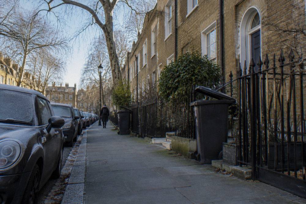 A narrow London residential street with brick terraced houses and parked cars