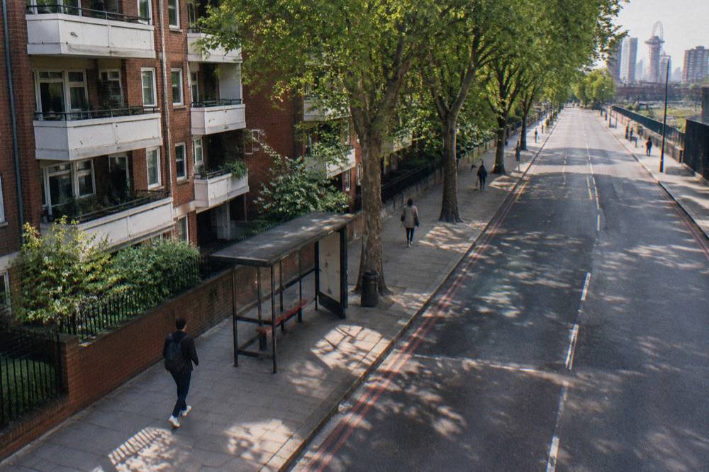 A wide London street with a red brick apartment building and trees along the pavement