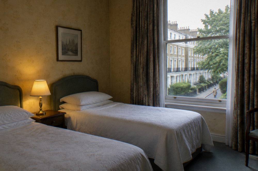A twin hotel room with two single beds and a bedside table lamp