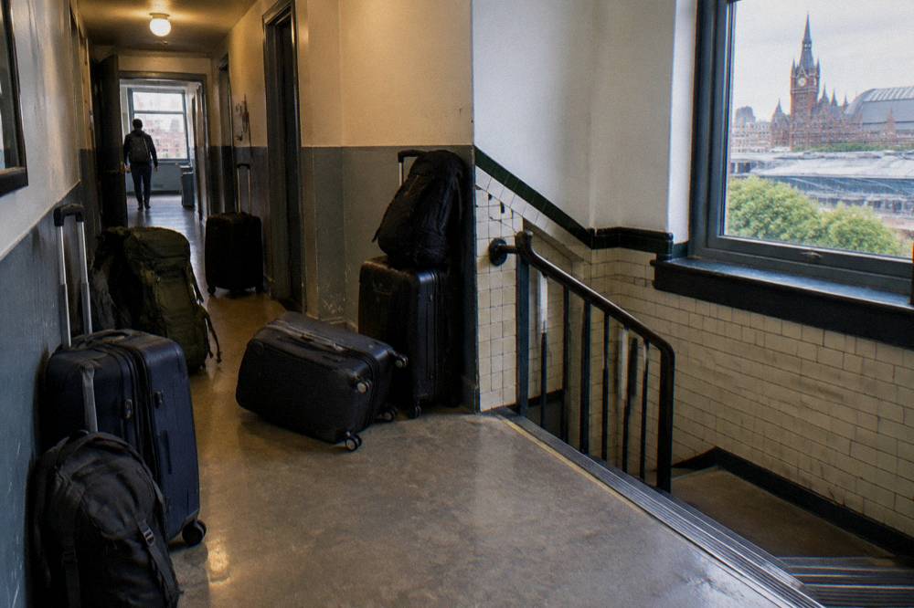 A row of suitcases and backpacks parked along a corridor wall beside a stairwell