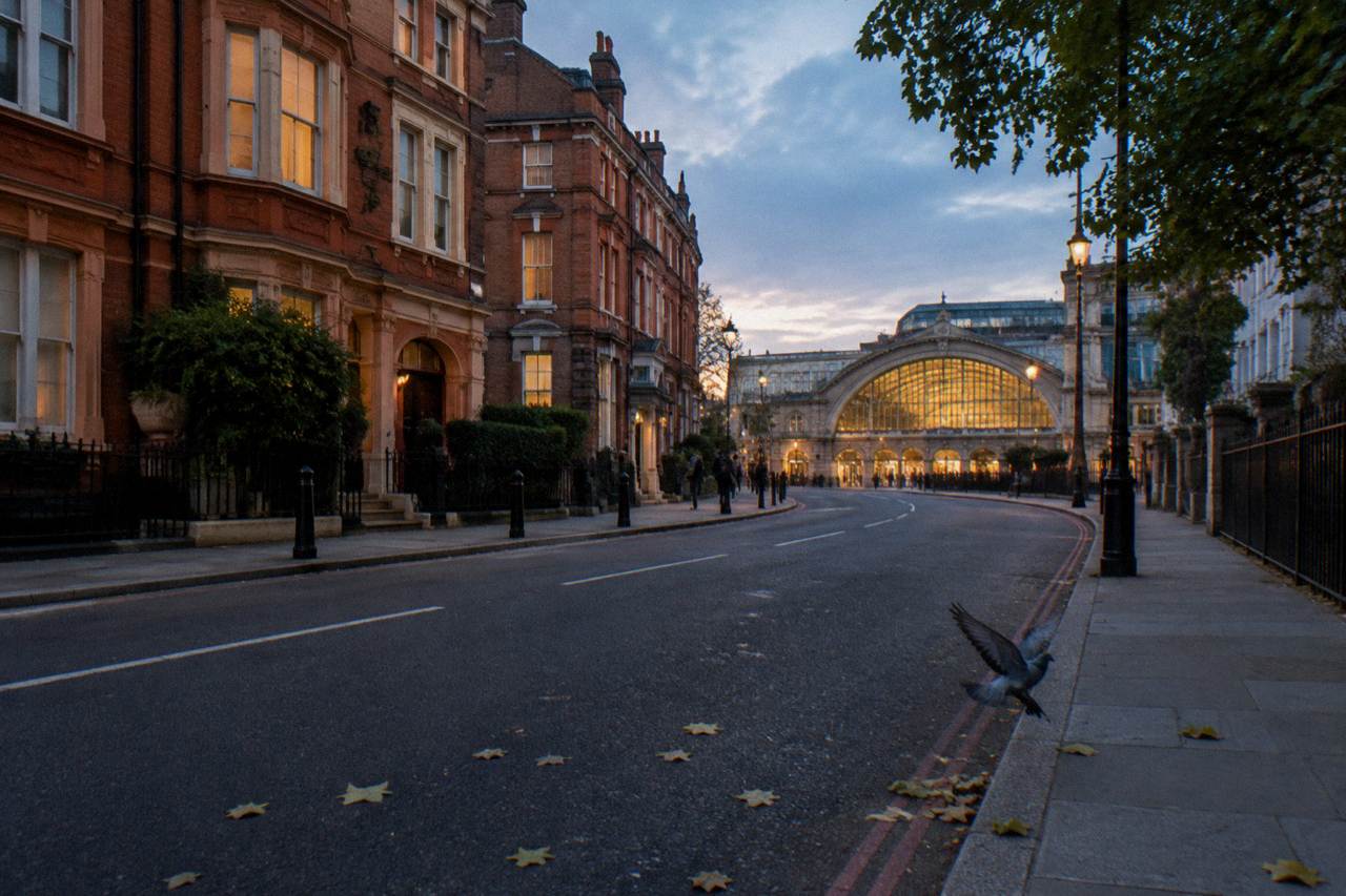 A London street at dusk with a terracotta terrace of small hotel facades and a lit station entrance beyond