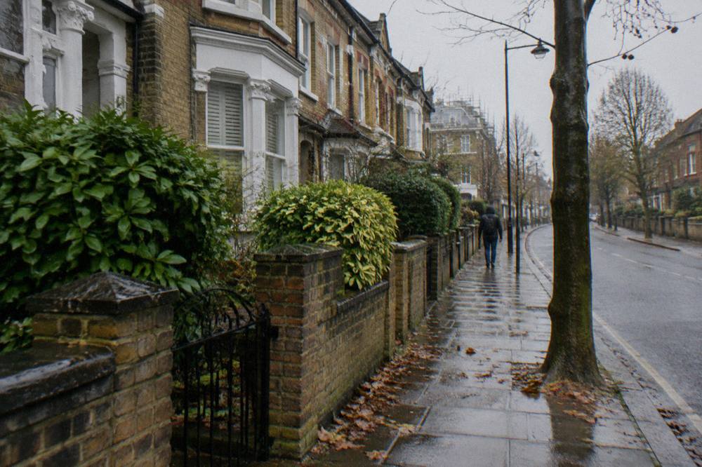 A narrow London residential street with brick terraced houses and parked cars