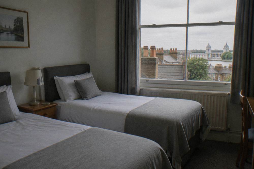 A twin hotel room with two single beds, bedside table and pale walls