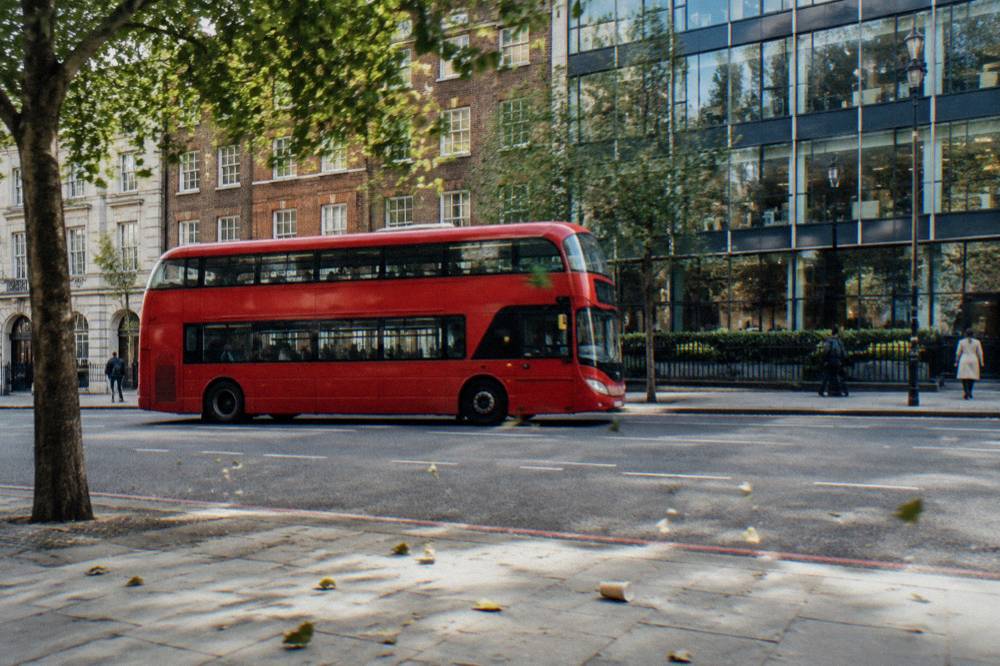 A red double decker bus on a London street with mixed brick and glass buildings behind