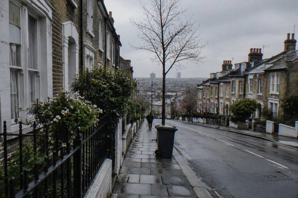 A London street with narrow terraced houses and parked cars under an overcast sky