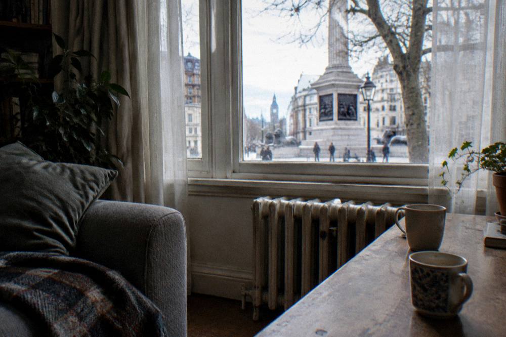 A sitting area in a small flat with a sofa, table and window with net curtains