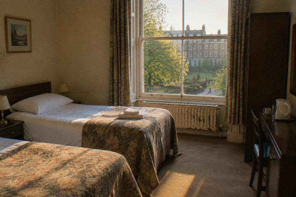 A twin hotel room with two single beds and a window in daylight