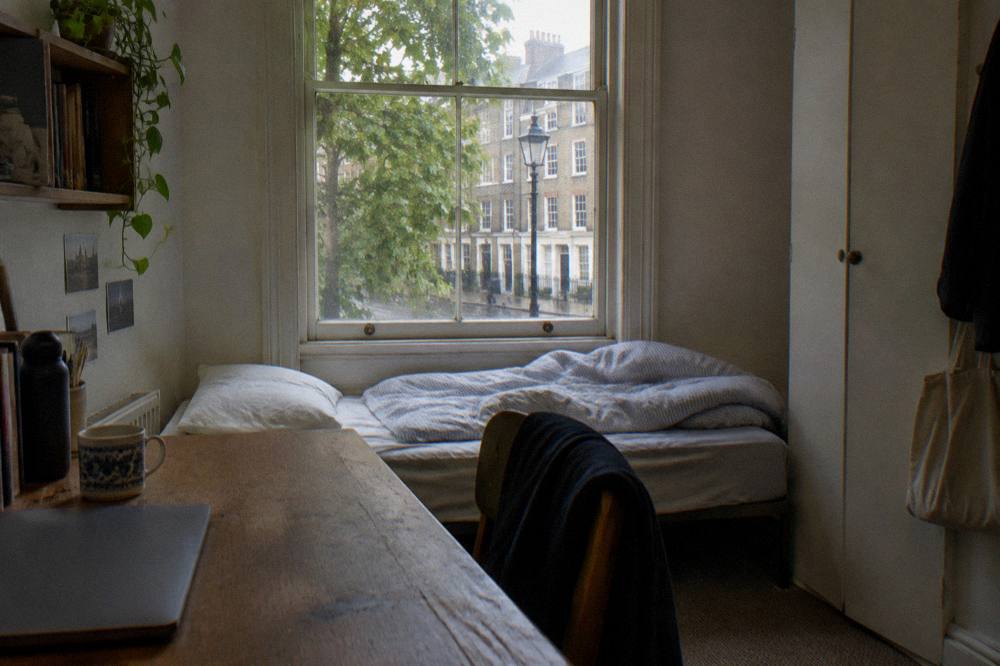 A small single hotel room with a bed, desk and window in daylight